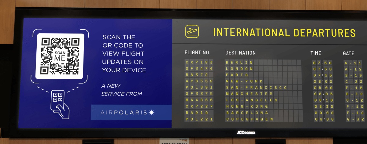 QR Code auf der Abflugtafel eines Flughafens mit der Aufforderung, ihn zu scannen, um aktuelle Flugdaten auf dem Handy anzuzeigen.