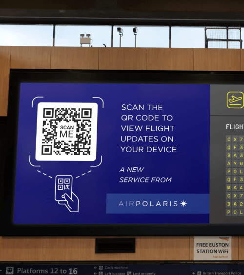QR Code auf der Abflugtafel eines Flughafens mit der Aufforderung, ihn zu scannen, um aktuelle Flugdaten auf dem Handy anzuzeigen.