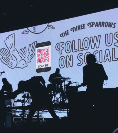 Bühnenanzeige bei einem Konzert mit einem QR Code, der die Social-Media-Kanäle einer Band verlinkt.
